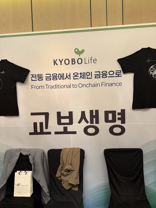 A promotional banner for 'KYOBO Life' with the slogan 'From Traditional to Onchain Finance' (전통 금융에서 온체인 금융으로) and '교보생명' (Kyobo Life) in large Korean text, displayed with merchandise including black t-shirts and clothing.