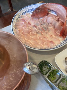 A plate of thinly sliced raw red fish sashimi served alongside dipping sauces and chopsticks.