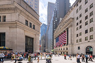 The image shows a bustling street scene outside the New York Stock Exchange, with a large American flag hanging prominently on the building's facade and crowds of pedestrians, including police officers, walking along the sidewalk. 

This connects to the post's themes of financial grinding, rule changes, and effort being wasted—evoking the tension of stock markets where sudden rule shifts can erase hard-won gains, much like being thwarted at a verification step after relentless grinding.