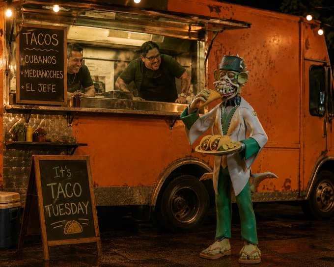 A night scene at an orange taco food truck with a chalkboard menu listing 'TACOS - CUBANOS - MEDIANOCHES - EL JEFE' and a 'It's TACO TUESDAY' sign, with a quirky mascot figure holding tacos out front.
