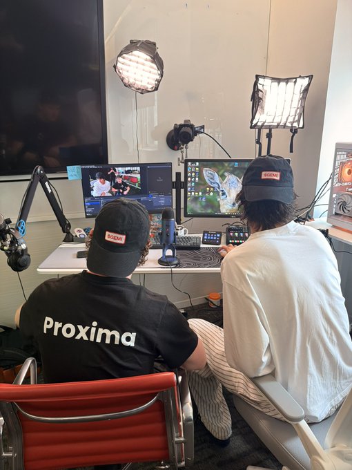 Two people wearing 'SCENE' branded caps sit at a desk with dual monitors, microphones, and studio lighting, with one wearing a shirt reading 'Proxima'.