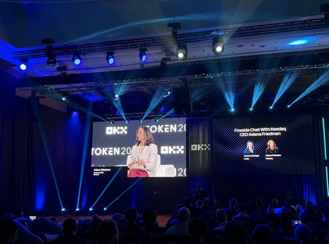A stage at the OKX TOKEN 2049 conference featuring a large screen showing a 'Fireside Chat With Nasdaq CEO Adena Friedman' panel.