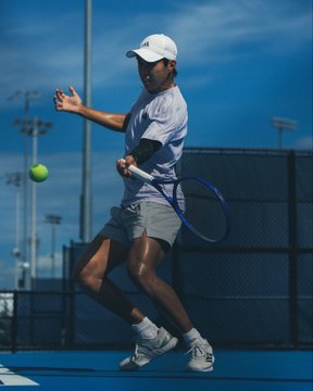 A tennis player in a white shirt and shorts swings a racket to hit an incoming ball on an outdoor court, an image illustrating the sports trading theme discussed in the post, which highlights a Polymarket trader profiting $2.4M with a 43% win rate.