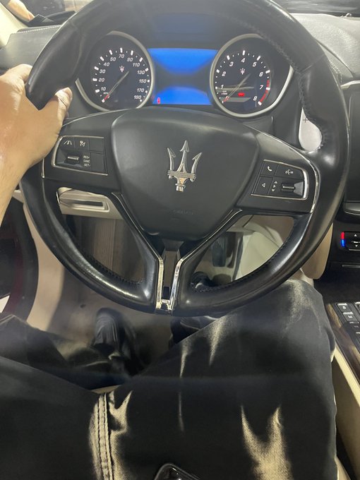 A first-person view from the driver's seat of a Maserati, showing the steering wheel with the iconic trident logo and the analog gauge cluster displaying the speedometer (up to 180 mph) and tachometer (up to 8,000 rpm) lit up in blue, fitting the "Gn bros" caption by giving a peek inside the luxury ride.