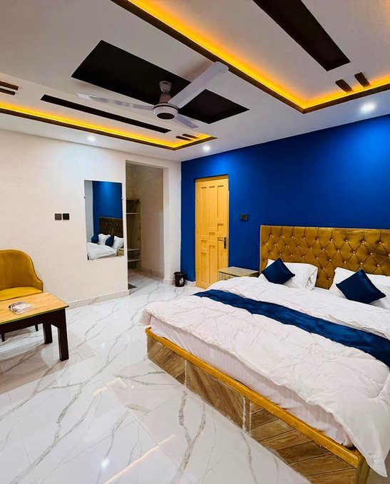 A luxurious hotel-style bedroom featuring a large bed with a tufted golden headboard, blue accent wall, and modern tray ceiling with LED lighting, paired with a sleek lounge area. The elegant, restful setting visually reinforces the post's message about quality sleep and wellness, aligning with @sleepagotchi's theme of building healthy sleep habits while owning personal wellness data.