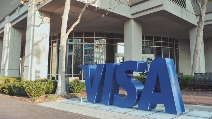 A large blue VISA sign stands outside a corporate building entrance.