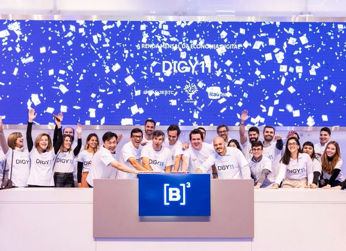 A celebratory group photo of people wearing white 'DiGY11' shirts at the '3ª RENDI MENSA DA ECONOMIA DIGITAL' event, with confetti falling and the [B]³ logo displayed on the central podium.
