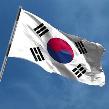 The national flag of South Korea waving against a blue sky, featuring the white background, central red and blue taegeuk symbol, and four black trigrams.