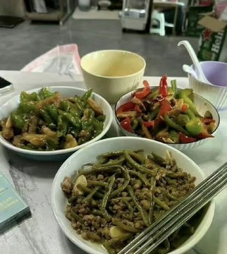 A table spread with three bowls of Chinese home-cooked dishes including green beans with meat, peppers with meat, and green beans, alongside a bowl of soup.