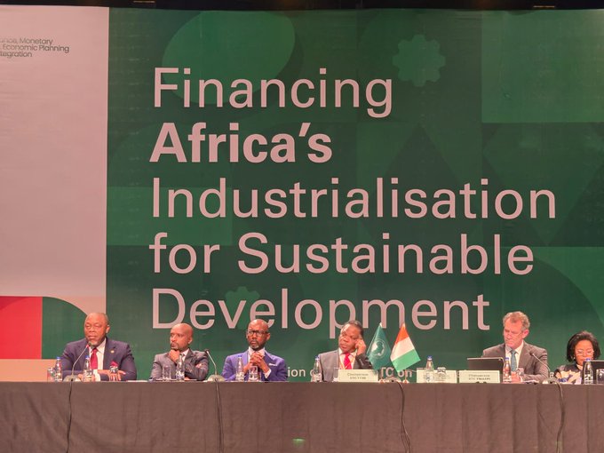 A panel of six individuals sits at a long table during a conference, with a large green backdrop displaying the title "Financing Africa's Industrialisation for Sustainable Development." The event appears to be hosted by the African Development Bank, with Côte d'Ivoire and African Union flags visible on the table.
