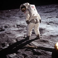 A historic photograph of an astronaut in a white spacesuit standing on the lunar surface with a flag planted in the soil.