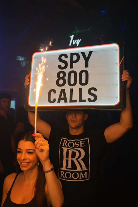 A woman holds a sparkler while a man behind her holds a sign reading 'SPY 800 CALLS' at a nightclub; the man wears a 'Rose Room' t-shirt.