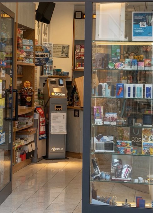 A Bitcoin ATM (Coinflip-branded, branded "bitcoin") stands inside a small shop in Bologna, Italy, surrounded by shelves of snacks and a glass display case of electronics. The machine, which supports transactions of up to €100,000 as noted on the nearby signage, directly illustrates the post's sighting of a Bitcoin machine in Bologna.