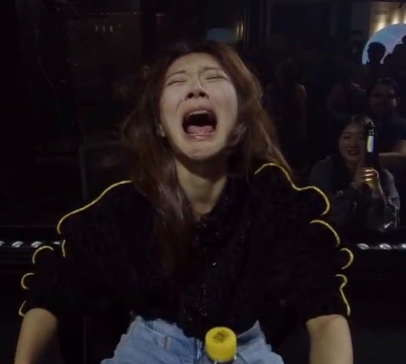 A woman with long brown hair, wearing a black ruffled top and jeans, is captured mid-laugh or scream with her mouth wide open and eyes squeezed shut, appearing to be in a dimly lit venue with other people in the background. The image conveys an intense, emotional reaction that visually echoes the post's mix of frustration and venting about the situation with @AbstractChain, despite the author claiming to keep their thoughts private.