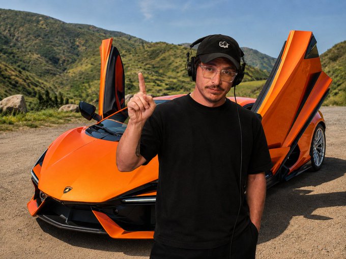 Opti stands in front of a bright orange Lamborghini with its scissor doors open, wearing headphones and a cap with the "SB" logo, gesturing upward while promoting his Simply Bitcoin Live course on how to purchase the car with Bitcoin.