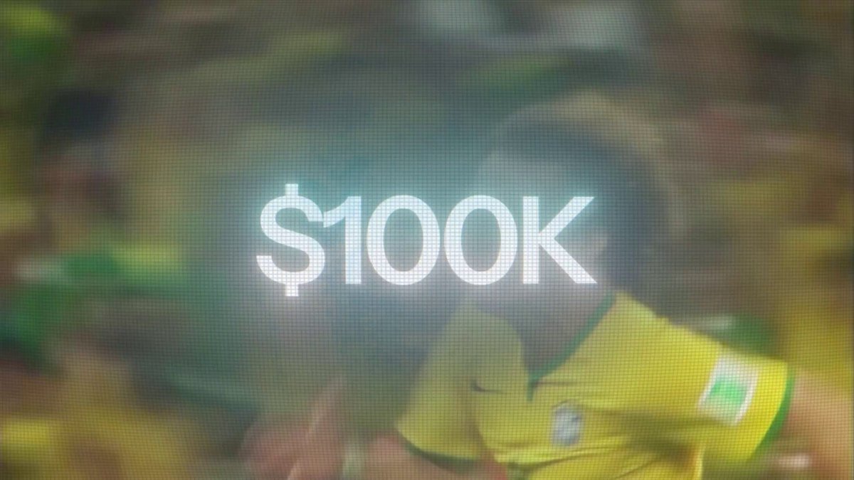 The image shows a scene of a soccer match with two teams, one wearing yellow jerseys and the other wearing green. The crowd appears to be very engaged and excited during the game. There are also several other people visible throughout the background of the image. A banner or advertisement is displayed in the foreground that reads "$100k", indicating some sort of prize or reward for a particular event, such as this soccer match.