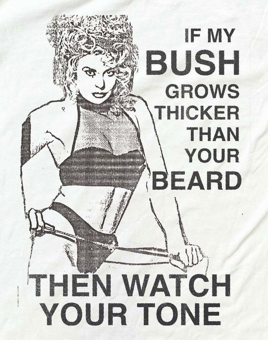 A graphic printed on fabric shows a black-and-white illustration of a woman in a bikini holding a sword, with bold text reading, 'IF MY BUSH GROWS THICKER THAN YOUR BEARD THEN WATCH YOUR TONE.'