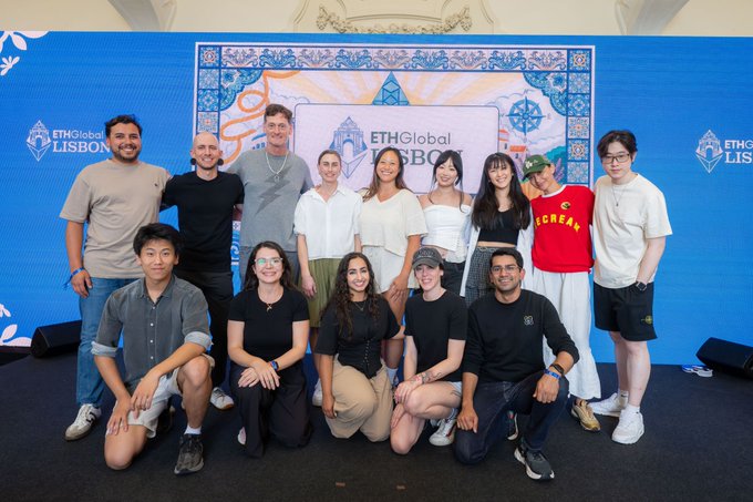 A group photo of approximately 13 people posing in front of a blue ETHGlobal Lisbon backdrop at an event.