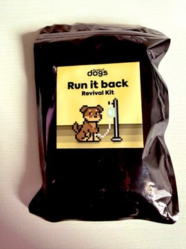 A dark brown coffee bag with a yellow label reading 'dogs Run it Back Revival Kit' featuring a cartoon dog peeing on a lamppost.