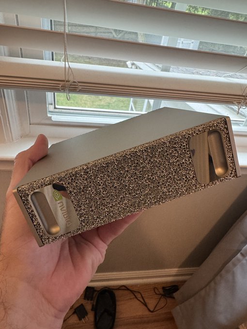 A hand holding a Nuibana product box with a gold-speckled textured interior, photographed near a window with blinds.