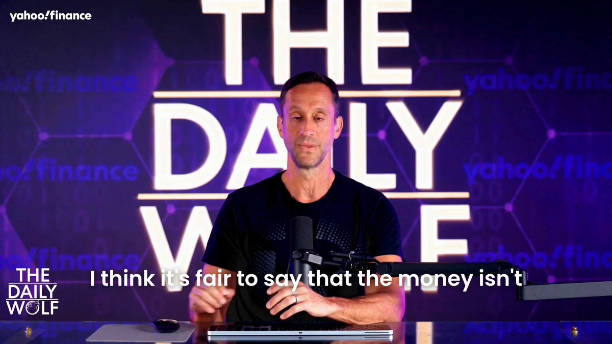 The image shows a man sitting at a desk with a microphone in front of him, suggesting that he might be hosting or participating in an interview or podcast discussion about cryptocurrency trading volume and market trends. The background features a purple wall with white text, which reads "The Daily Wolf" and "I think it's fair to say that the money isn't leaving crypto right now, it' s actually rotating inside it. All the hedge funds went and unfollowed Bitcoin and slid into Hyperliquid's DMs". This quote from the post emphasizes the current state of cryptocurrency trading volume and highlights how big money is being invested in Bitcoin and other cryptocurrencies at present.