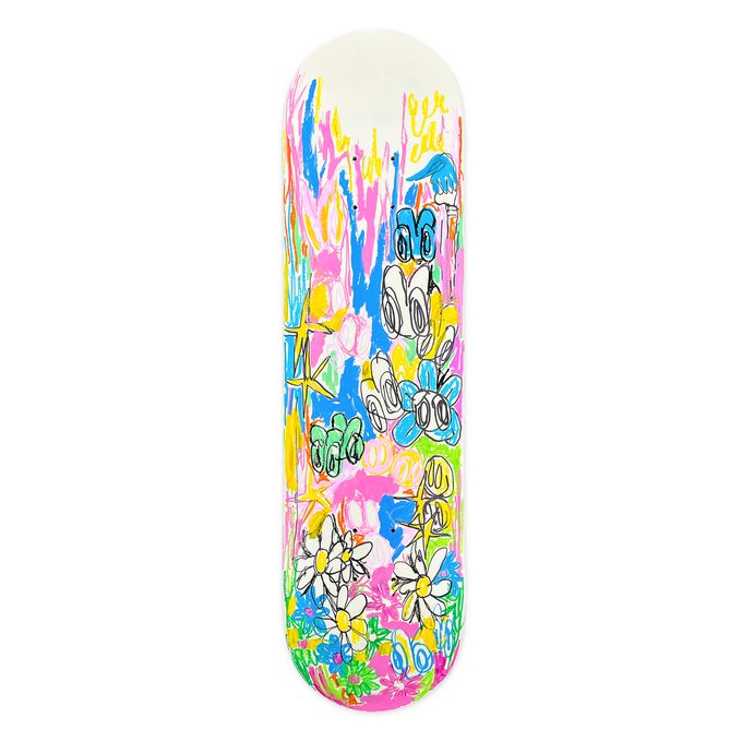 A skateboard deck with a colorful, doodle-style graphic design featuring flowers, stars, and dripping paint in pink, blue, yellow, and green, with a stylized signature near the top.