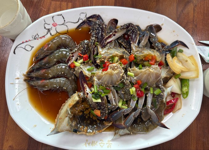A plate of marinated raw crab (간게장 style) garnished with red chili peppers, green onions, and green peppers, served with lemon slices in a soy-based sauce.