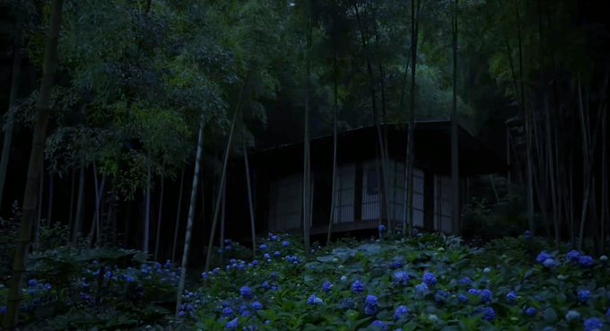 A dark, atmospheric image of a traditional Japanese building nestled within a bamboo forest, surrounded by blue hydrangea flowers in the foreground.
