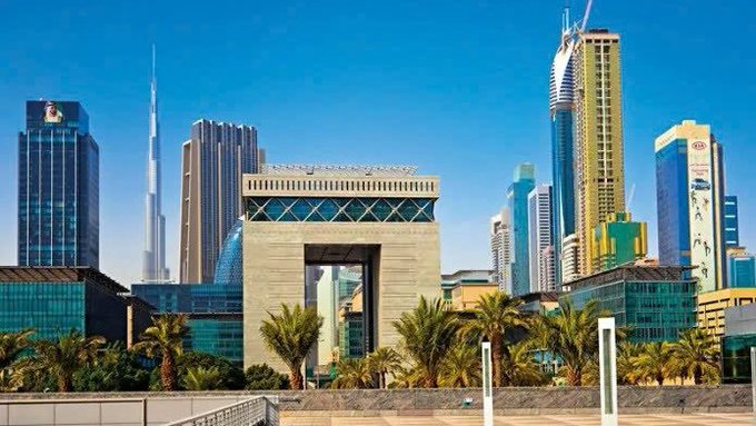 A view of the Dubai skyline featuring the Dubai Frame structure prominently in the foreground, with the Burj Khalifa and other skyscrapers visible behind it under a clear blue sky.