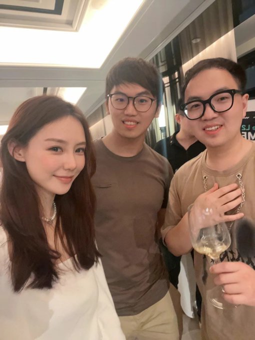 Three young professionals pose together at a social gathering, with the man on the right holding a wine glass and the woman on the left wearing a white blouse and pearl necklace. The warm indoor setting with modern lighting evokes the celebratory Bybit dinner vibe described in the caption, marking a meaningful milestone three years after first meeting at the HK Web3 Carnival.