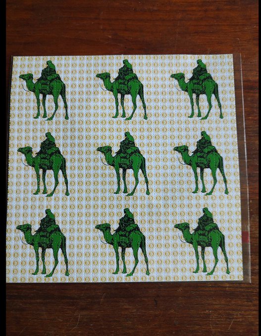 A sheet of green camel stickers arranged in a grid pattern, each showing a figure riding a camel, resting on a wooden surface.