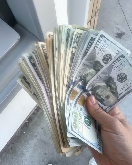A hand fans out a thick stack of US $100 bills on a sidewalk, visually reinforcing the caption's message that cash sitting idle belongs in an account—working and earning—rather than being held back.