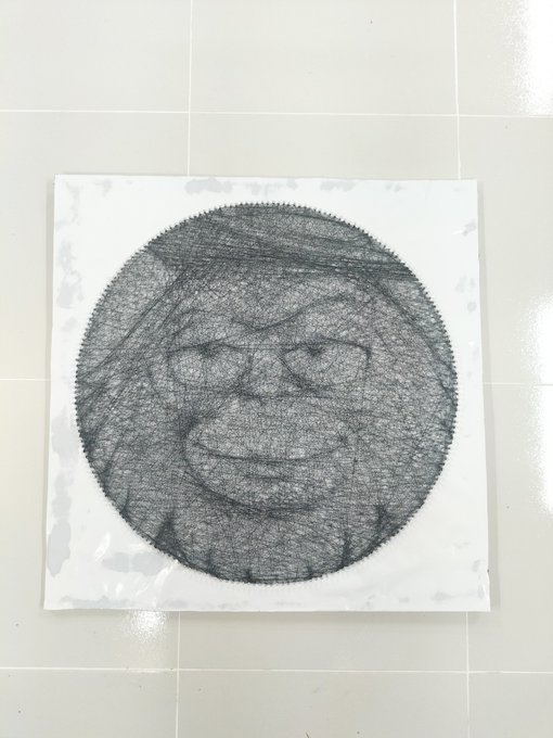 A pencil drawing on paper lying on a tiled floor, depicting a smiling face with glasses rendered as a circular scribbled pattern on the page.