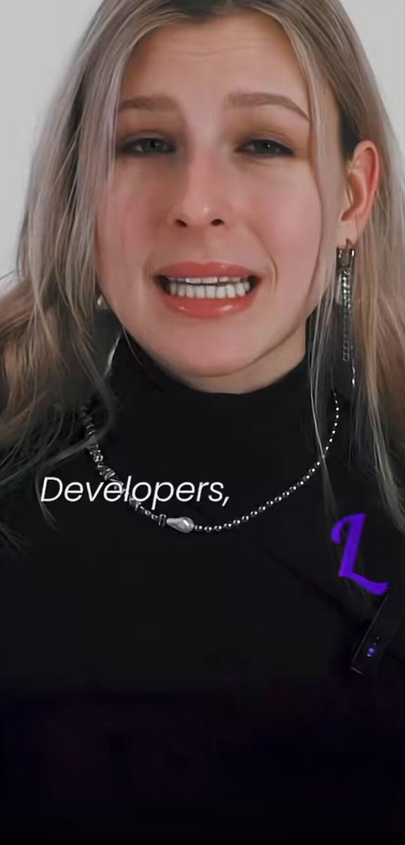 The image features a woman with blonde hair wearing a black top and has a purple letter "L" on her shirt. The caption of the image reads, "Developers." This suggests that the photo might be related to a discussion or review about software development or an application being developed by developers.