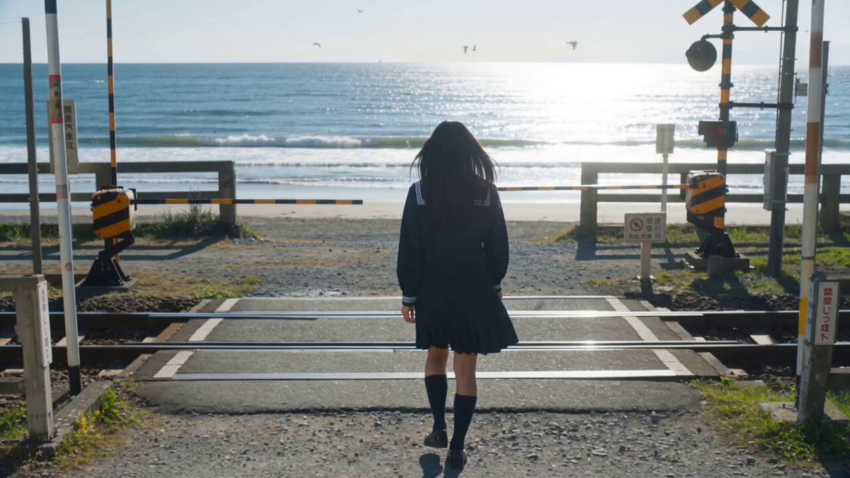 The image shows a woman walking across a road or bridge, wearing a school uniform with black socks and a skirt. The background features a beach scene with ocean waves and birds flying above them. There are also two traffic lights visible in the image. The text on the post reads "Good morning CT Can i get GM back? You're still early in Web3 today. @wallchain @3look_io @XOOBNetwork". This message seems to be related to a conversation or discussion about the current time, possibly involving cryptocurrency trading or other online activities.
