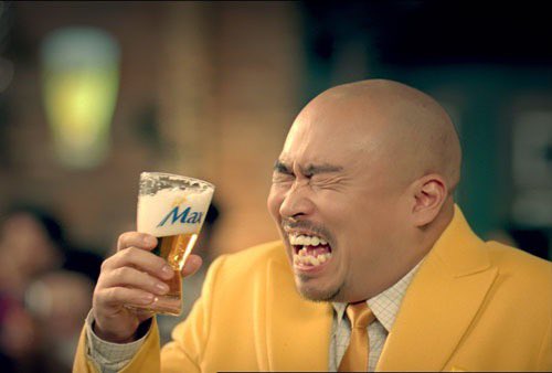 A bald man in a yellow suit grimaces while holding a glass of "Maes" beer, mouth open in an enthusiastic shout—visually capturing the "glory" and celebratory energy of the poster's dedication to $ABCL shareholders.