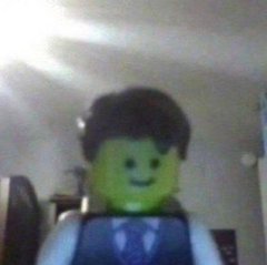 A low-quality webcam image displays a person wearing a Lego minifigure head filter over their face in a dimly lit room.