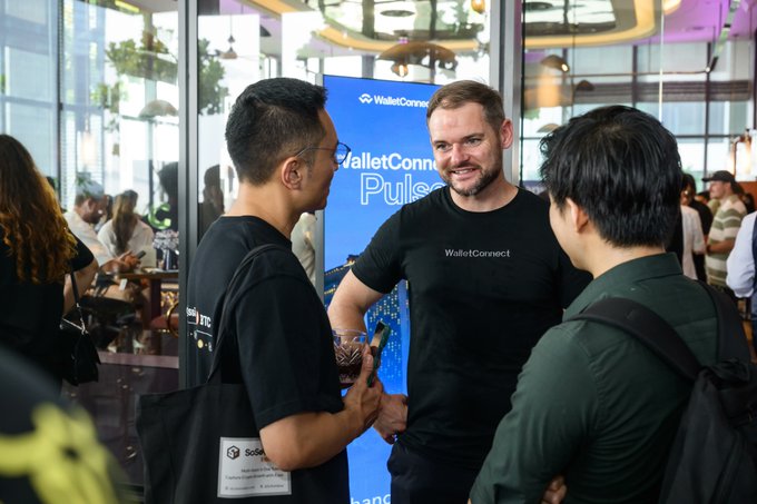 Three men wearing black "WalletConnect" shirts converse at the WalletConnect Pulse event, with a branded banner visible in the background, capturing the collaborative networking atmosphere highlighted in the post about bringing industry leaders together alongside Token2049.