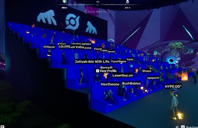 A screenshot from a video game shows a crowd of player avatars gathered on a blue tiered structure in a location labeled 'Pulse District,' with usernames visible like 'LOLERS,' 'Bannett,' 'LaserGuyum,' 'BushBabies,' and 'HYPE.06'.