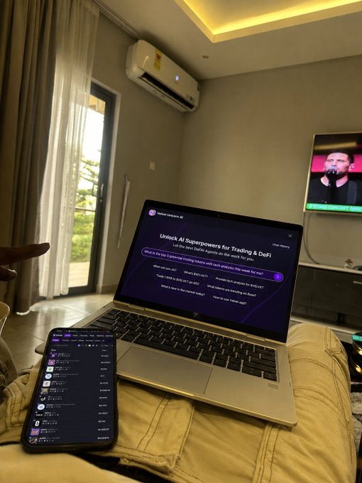 A laptop sits on a beige couch displaying a chat interface titled 'Unlock AI Superpowers for Trading & DeFi', with a smartphone showing a crypto app beside it and a TV in the background.