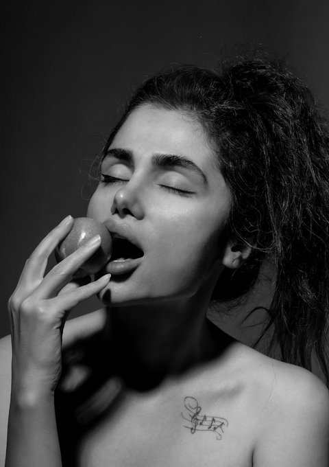 A black-and-white artistic portrait shows a woman with closed eyes about to bite into a glossy apple, with the figure "Pleasure" visible in small handwritten text on her shoulder—matching her NFT piece titled "Pleasure" from the "Archetypes" collection. The sensual, intimate imagery captures the essence of the "pleasure archetype" through the simple yet evocative act of tasting an apple.