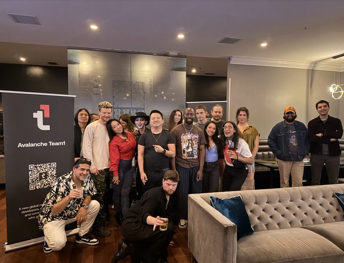 A group photo of a diverse team posing together at an indoor event, with a banner on the left displaying the Avalanche Team1 logo, a QR code, and text reading 'A new global stablecoin, designed for who...'.