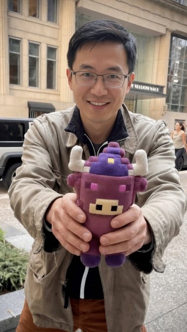 A smiling man wearing glasses and a beige jacket stands on a city street, holding up a purple plush toy with white horns.