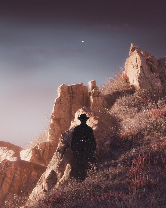Artistic photo of a silhouetted figure wearing a starry-patterned cloak standing among rocky terrain under a twilight sky with a visible celestial body.