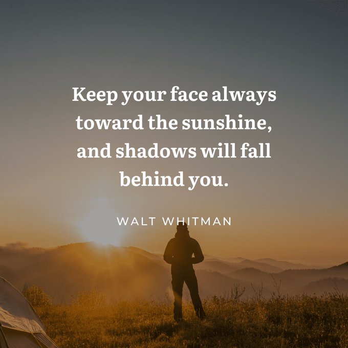 An inspirational quote by Walt Whitman reads, 'Keep your face always toward the sunshine, and shadows will fall behind you,' overlaid on a silhouette of a person watching a mountain sunrise.