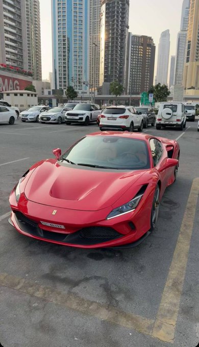 A red Ferrari F8 sports car is parked on a city street lined with skyscrapers. The post appears to be a comment directed at a Formula 1 race broadcast, with the Ferrari serving as a subtle reference to the Italian team's involvement in the sport.