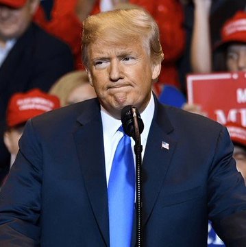 A photo of Donald Trump speaking at a microphone, wearing a dark suit with a blue tie and American flag pin, with supporters in red MAGA hats visible in the background.