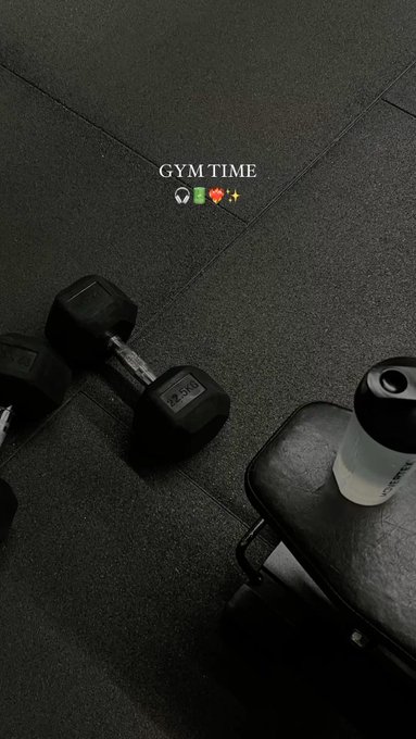 A dark gym floor with dumbbells, a workout bench, and a water bottle, overlaid with the text 'GYM TIME' and small icons including a soccer ball, dumbbell, heart, and sparkle.