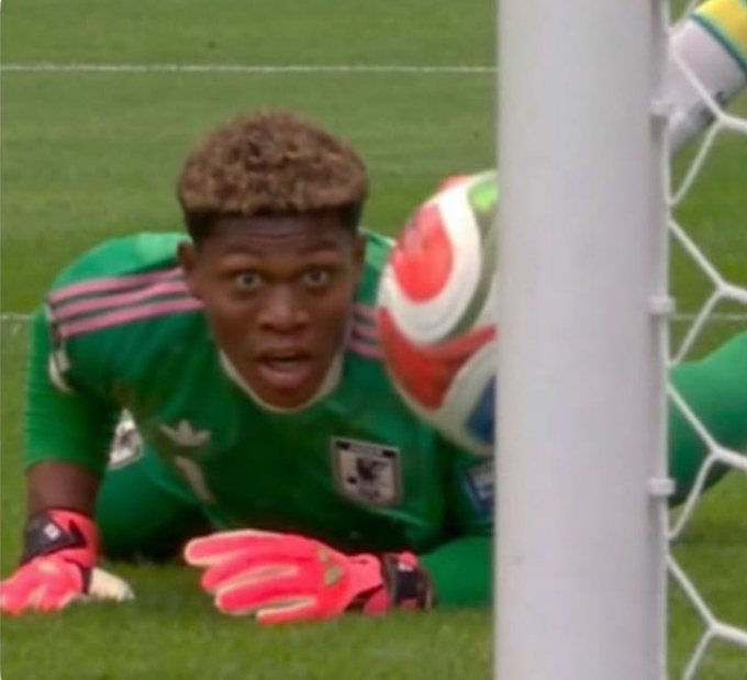 A young soccer goalkeeper in a green Mexico jersey with pink gloves watches in stunned silence as a ball sails past his head toward the net — perfectly capturing the wide-eyed, doomed expression of someone about to get scored on.