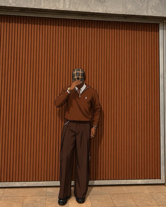A person wearing a brown sweatshirt and wide-leg brown pants stands against a rust-colored corrugated metal wall, holding up a plaid flat cap to obscure their face. The earthy, monochromatic styling pairs well with a relaxed "gm, happy friday" greeting, evoking a cozy yet confident weekend vibe.